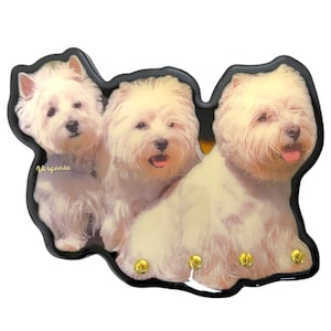 Może przedstawiać: Dekoracyjny brelok do kluczy z trzema zdjęciami West Highland White Terrier. Brelok jest czarny ze złotymi haczykami. Na breloku widnieje napis "Virginia".