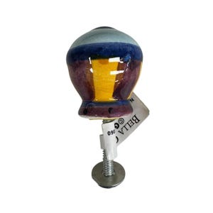 May include: A ceramic cabinet knob with a rounded top and a glossy finish. The surface features horizontal bands of light blue, dark blue, yellow, and purple. A metal screw and washer are attached to the base, along with a white paper tag labeled BELLA.