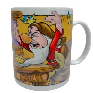 May include: White ceramic mug featuring an illustration of Grumpy from Snow White. The design shows Grumpy in a red shirt, brown hair, and a white beard, with blue birds and a yellow background. The mug has a white handle.