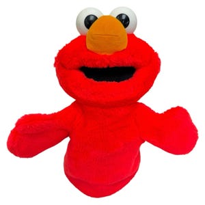 May include: A bright red plush hand puppet featuring a large orange nose, two prominent white eyes with black pupils, and a wide open mouth. The puppet is covered in soft, fuzzy red fabric and has two outstretched arms extending from the sides.