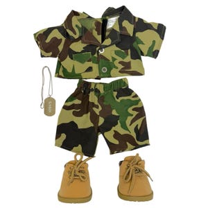 Op de afbeelding: Een camouflageprint overhemd met korte mouwen, knoopsluiting en twee borstzakken, een bijpassende camouflageprint short met elastische tailleband, een paar beige veterschoenen en een zilverkleurige dogtag ketting.