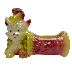 May include: A vintage ceramic planter in the shape of a cat. The cat is yellow, pink, and red with blue eyes. The planter is a barrel shape with a red and yellow gradient and a floral design.