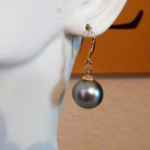 May include: A pair of gold earrings with a single black pearl drop on each earring. The pearls are round and have a smooth, glossy finish.
