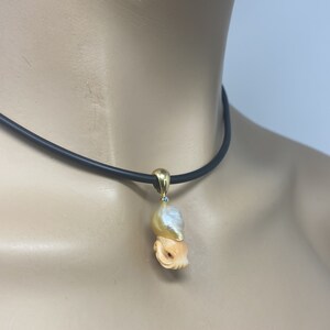 May include: A gold necklace with a carved shell pendant featuring a pearl and a small turquoise gemstone. The pendant is shaped like an octopus.