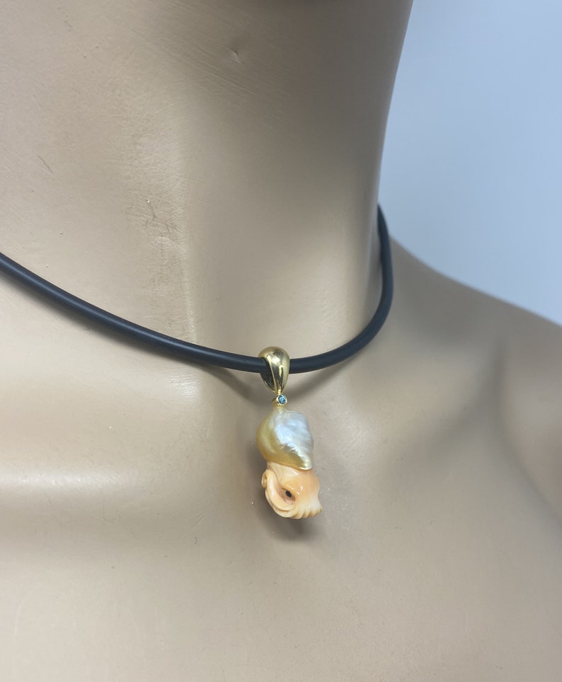 May include: A gold necklace with a carved shell pendant featuring a pearl and a small turquoise gemstone. The pendant is shaped like an octopus.