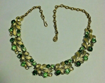May include: A gold tone necklace with a chain and a design of green leaves and rhinestones.