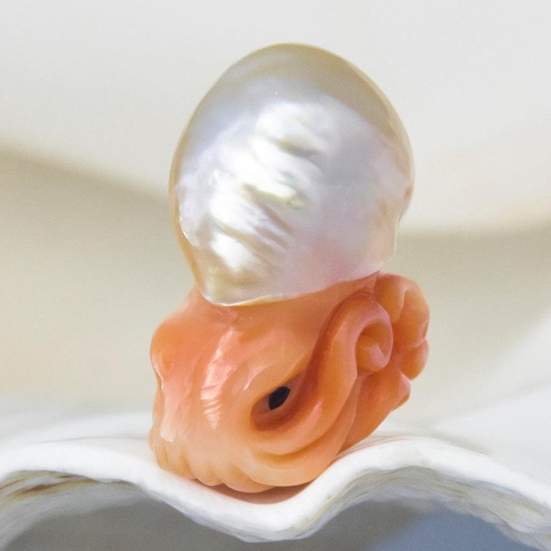 May include: A carved coral octopus with a large, white, iridescent pearl on top. The octopus is a light orange colour and has detailed carvings.