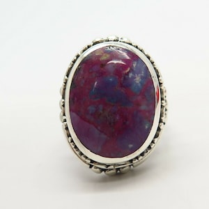 May include: A silver ring with an oval-shaped purple and pink gemstone set in a decorative silver bezel.