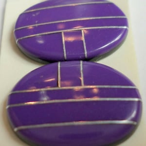 May include: Two purple and silver round buttons with a geometric design. The buttons have a shiny finish and are perfect for adding a touch of color and style to any project.