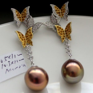 Puede incluir: Un par de pendientes de plata con una perla colgante y tres abalorios de mariposa. Las mariposas son doradas con piedras amarillas y transparentes.