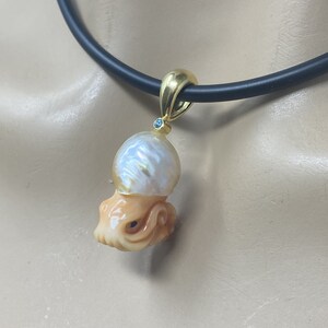 May include: A gold pendant necklace featuring a carved octopus and a large pearl. The pearl is iridescent and has a blue gemstone set in the top.