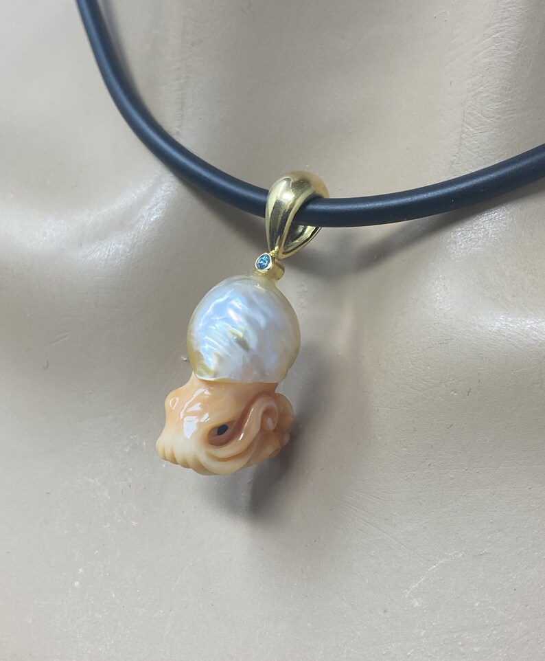 May include: A gold pendant necklace featuring a carved octopus and a large pearl. The pearl is iridescent and has a blue gemstone set in the top.