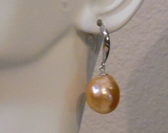 May include: A pair of silver hoop earrings with a single, large, peach-colored pearl dangling from each hoop.