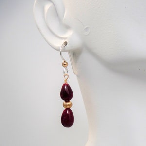 May include: A pair of dangle earrings with two teardrop-shaped red gemstone beads and gold accents.
