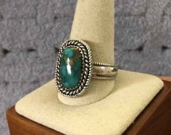May include: A silver ring with a large oval turquoise stone set in a silver bezel. The ring has a braided design around the stone and the band.