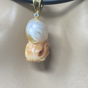 May include: A gold pendant necklace featuring a carved pearl and a blue gemstone. The pendant is shaped like an octopus.