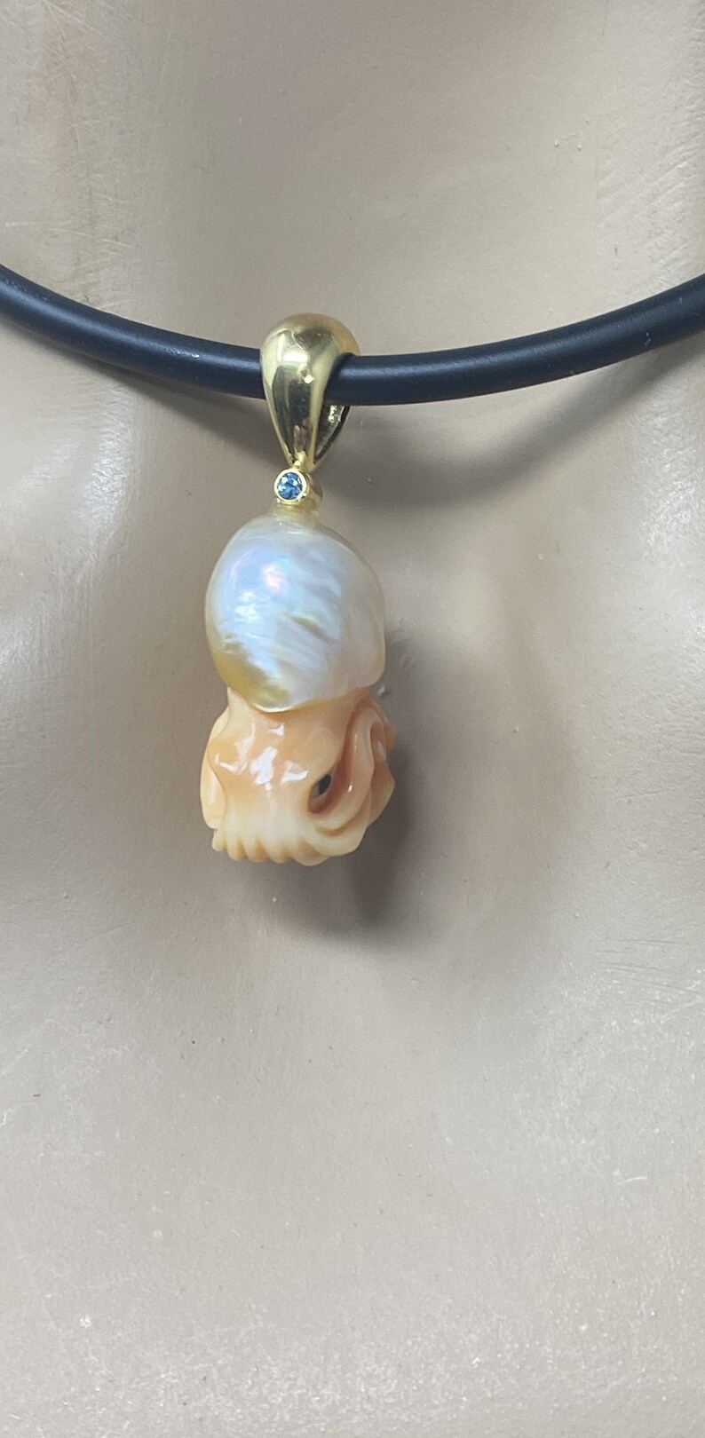 May include: A gold pendant necklace featuring a carved pearl and a blue gemstone. The pendant is shaped like an octopus.