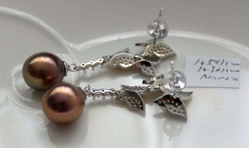 Puede incluir: Un par de pendientes de plata con una perla marr&oacute;n y un dise&ntilde;o de hojas. Las hojas est&aacute;n incrustadas con peque&ntilde;as piedras transparentes.