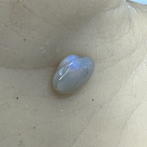 May include: A smooth, oval-shaped, iridescent gemstone with a light blue hue.