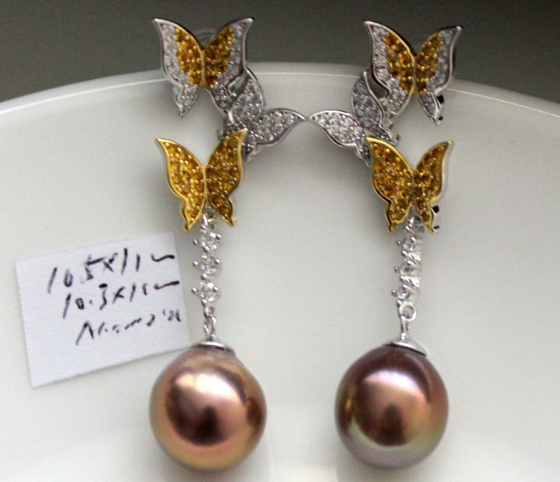 Puede incluir: Un par de pendientes colgantes con dise&ntilde;o de mariposa. Cada pendiente tiene dos mariposas con piedras amarillas y transparentes, y una perla marr&oacute;n.