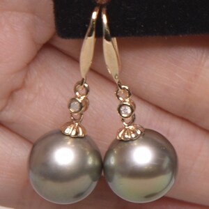 May include: A pair of gold dangle earrings with a single diamond accent on each earring. The earrings feature a large, round, dark gray pearl.