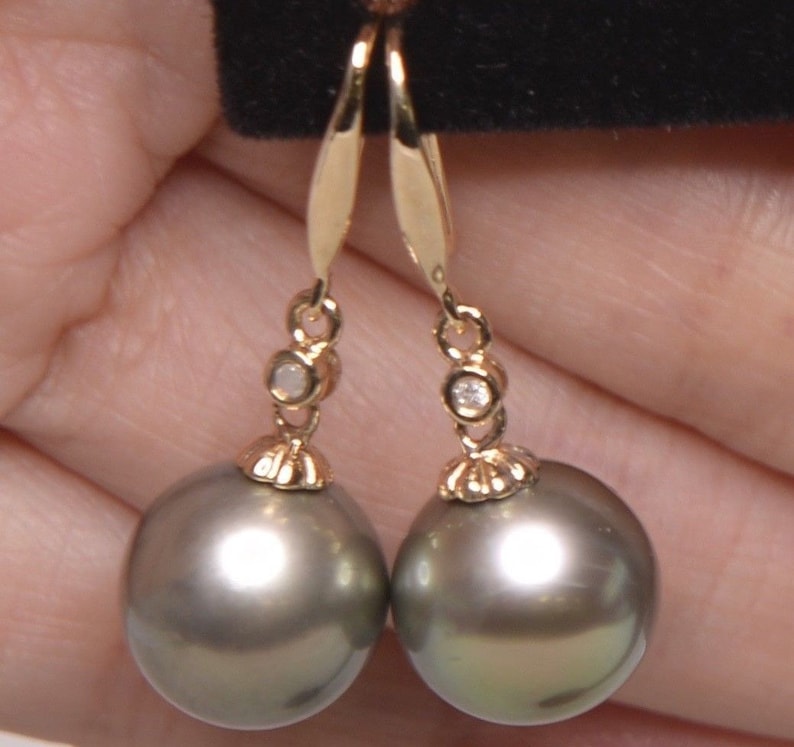 May include: A pair of gold dangle earrings with a single diamond accent on each earring. The earrings feature a large, round, dark gray pearl.