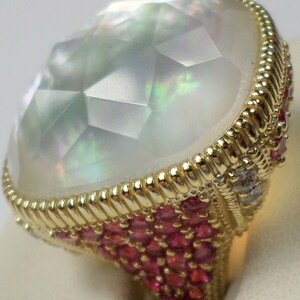 May include: A ring with a large, faceted, iridescent white gemstone surrounded by a band of small red gemstones and a single diamond.