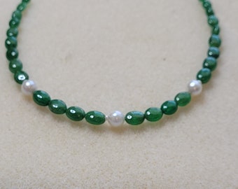 May include: A green and white beaded necklace with oval-shaped beads. The necklace has a pattern of alternating green and white beads.