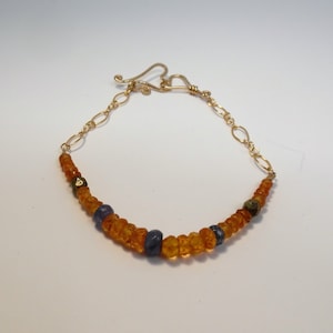 May include: A gold chain bracelet with amber and blue gemstone beads. The clasp is a heart shape.