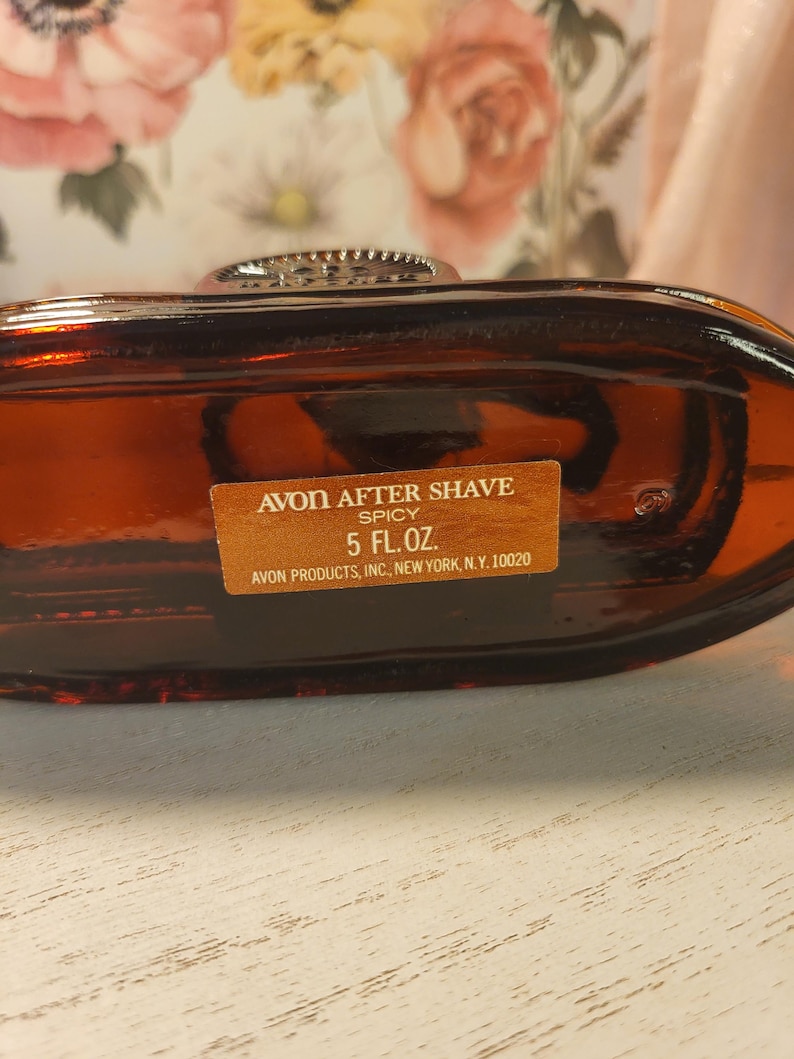 May include: A vintage Avon After Shave bottle in a rich amber color. The label reads "Spicy" and "5 FL.OZ." The bottle has a decorative silver-toned cap. The text "AVON PRODUCTS, INC, NEW YORK, N.Y. 10020" is also visible.