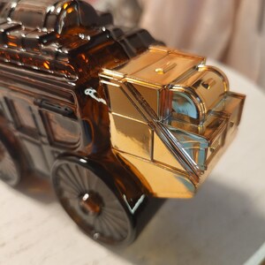 May include: A decorative amber glass stagecoach with gold-colored accents. The stagecoach features detailed wheels and a shiny gold roof. The design is reminiscent of vintage transportation.