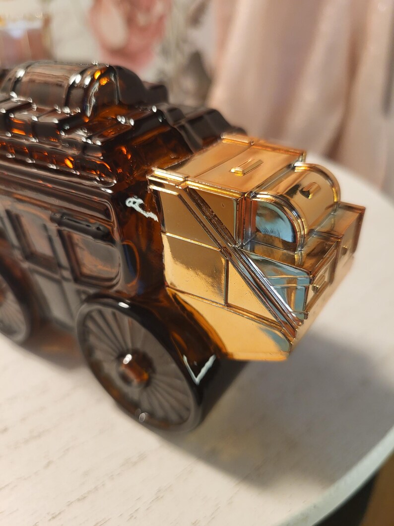 May include: A decorative amber glass stagecoach with gold-colored accents. The stagecoach features detailed wheels and a shiny gold roof. The design is reminiscent of vintage transportation.