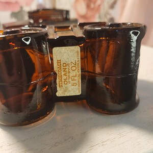 May include: Amber-colored glass bottles of Stagecoach Oland aftershave. The bottles are arranged on a white surface. The label reads "STAGECOACH OLAND AFTER SHAVE 5 FL. OZ."
