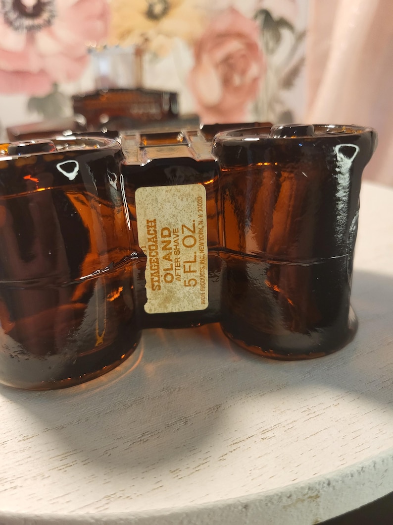 May include: Amber-colored glass bottles of Stagecoach Oland aftershave. The bottles are arranged on a white surface. The label reads "STAGECOACH OLAND AFTER SHAVE 5 FL. OZ."