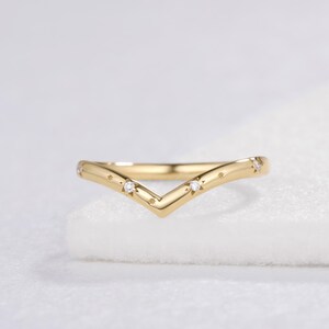 May include: A gold V-shaped ring featuring a polished band with a chevron silhouette. The ring is accented with small, clear, round-cut stones set within engraved star-shaped motifs spaced evenly along the top surface of the metal band.