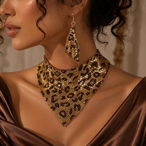 May include: Gold-toned necklace and earring set with a leopard print design. The necklace is a choker style, and the earrings are a matching, dangling shape. The jewelry is worn against a brown satin fabric.