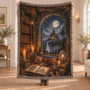 Pode incluir: Uma manta tecida apresentando uma cena de fantasia detalhada de uma biblioteca com uma grande janela em arco com vista para um castelo ao luar, uma cachoeira e uma floresta. O design inclui pilhas de livros, velas acesas e um gato.