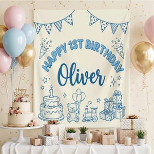 May include: A birthday backdrop with the text "Happy 1st Birthday Oliver" in blue, featuring illustrations of a cake, gifts, a teddy bear, and a train. Balloons in gold, pink, and blue are visible, alongside a decorated cake.