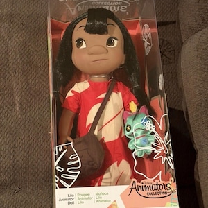 Puede incluir: Mu&ntilde;eca Lilo de la colecci&oacute;n Disney Animators en una caja transparente. La mu&ntilde;eca tiene cabello negro, ojos marrones y viste un vestido rojo con estampados florales blancos. Un bolso marr&oacute;n cuelga de su hombro y se incluye un peluche de Stitch.
