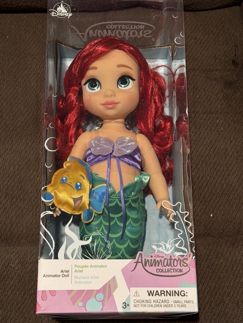 Puede incluir: Mu&ntilde;eca Ariel de la colecci&oacute;n Disney Animators. La mu&ntilde;eca tiene cabello rojo, ojos azules y viste un top morado y una cola de sirena verde. Incluye un peluche de Flounder. Empaquetada en una caja transparente.