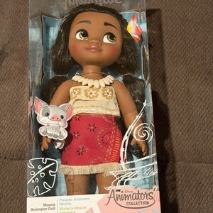 Puede incluir: Mu&ntilde;eca Moana de la colecci&oacute;n Disney Animators en una caja de pl&aacute;stico transparente. La mu&ntilde;eca tiene cabello oscuro, ojos marrones y un accesorio floral para el cabello. Viste un top beige, una falda roja con estampados florales blancos y un collar de conchas. Incluye un cerdito.