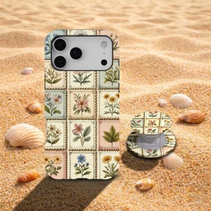 Puede incluir: Una funda de teléfono y un agarre a juego con un diseño floral. La funda presenta una cuadrícula de diseños de sellos postales vintage con varias flores. El agarre está abierto y tiene un patrón floral similar. Sobre arena.