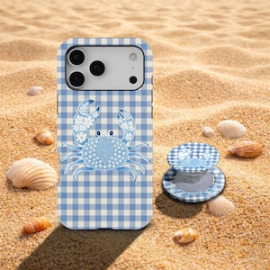 May include: A light blue and white gingham patterned smartphone case and a matching circular collapsible phone grip. The case features a central blue crab illustration decorated with white floral patterns on its shell and claws.