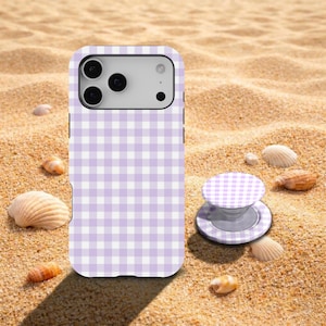 Peut inclure: Coque de téléphone et support assorti à motif vichy lilas et blanc. L'ensemble est posé sur du sable, avec des coquillages éparpillés autour.