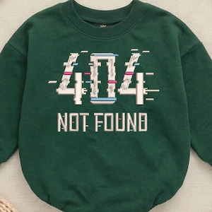 Könnte beinhalten: Waldgrüner Baby-Body mit langen Ärmeln. Auf der Vorderseite steht der Text "404 NOT FOUND" in Weiß mit einem Glitch-Effekt. Der Body besteht aus einem weichen Material und ist auf Komfort ausgelegt.