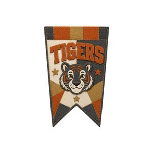 Peut inclure: Une bannière fanion en feutrine affichant le mot TIGERS en lettres capitales orange sur le haut. Sous le texte se trouve une illustration centrée d'une tête de tigre aux détails noirs, blancs et orange. Le fond présente un motif géométrique en étoile.