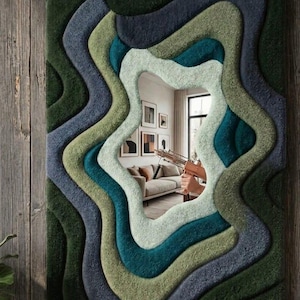 May include: A rectangular wall mirror featuring a thick, tufted, multi-layered frame with wavy, organic contours. The frame displays a gradient of deep forest green, teal, sage, and slate blue tones, creating a textured, topographical appearance.