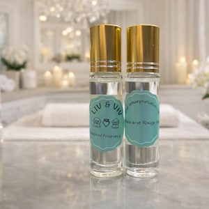 May include: Two clear glass roll-on perfume bottles with gold caps and light blue labels. The labels read "LIV & VIV" and "Interpretation of Baccarat Rouge 540". The bottles are on a marble surface.