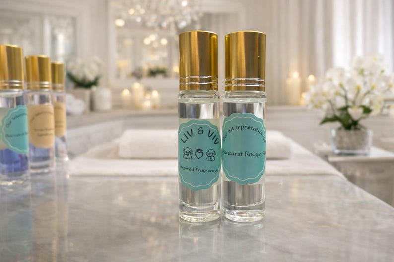 Puede incluir: Dos frascos de perfume roll-on de vidrio transparente con tapas doradas y etiquetas celeste claro. Las etiquetas dicen "LIV & VIV" y "Interpretation of Baccarat Rouge 540". Los frascos est&aacute;n sobre una superficie de m&aacute;rmol.