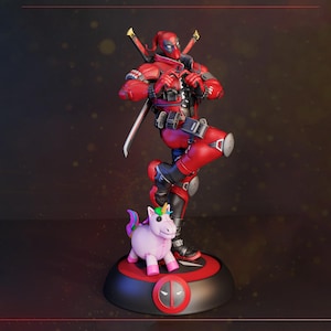 Puede incluir: Una figura de Deadpool con traje rojo y negro y dos katanas en la espalda, formando un corazón con las manos. Un pequeño juguete de unicornio rosa claro se encuentra a los pies sobre una base circular negra y roja con el logo de Deadpool.
